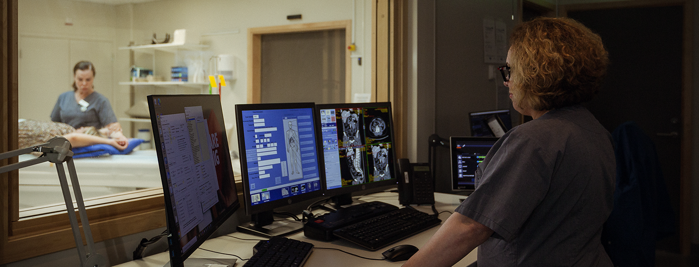 Röntgensköterska granskar bilder från kontrollrum under pågående datortomografiundersökning.